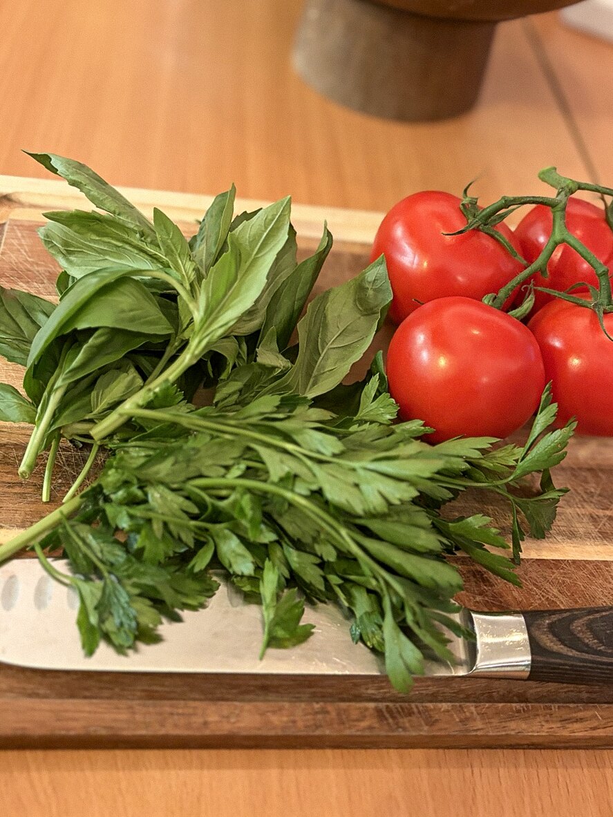 Fresh tomatoes, basil, and parsley on a cutting board